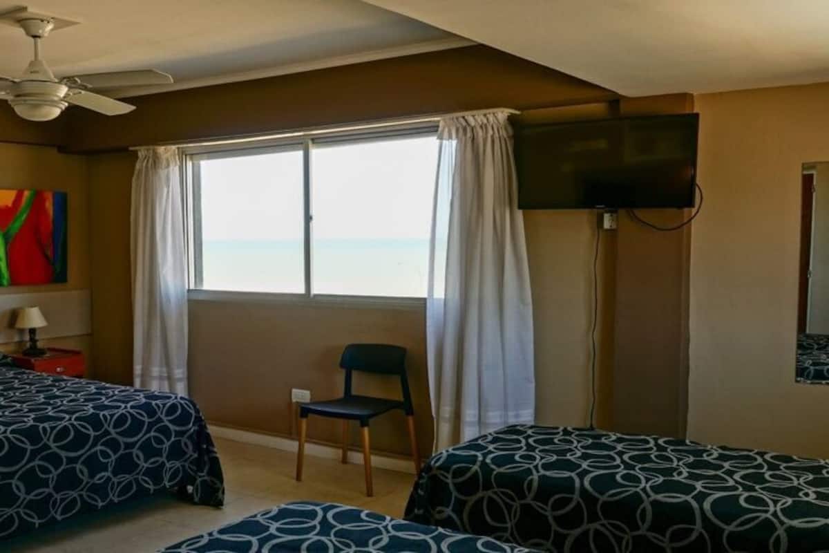 A hotel room with two beds, a ceiling fan, a TV, a window with curtains, and a chair.
