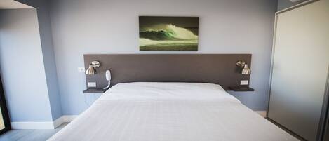 Ein modernes Hotelzimmer mit einem großen Bett, einem an der Wand befestigten Kunstwerk über dem Bett, Nachttischlampen und einem Kleiderschrank.