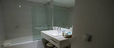 A modern bathroom with a glass-enclosed shower, a white sink with a mirror, and a built-in shelf with towels.