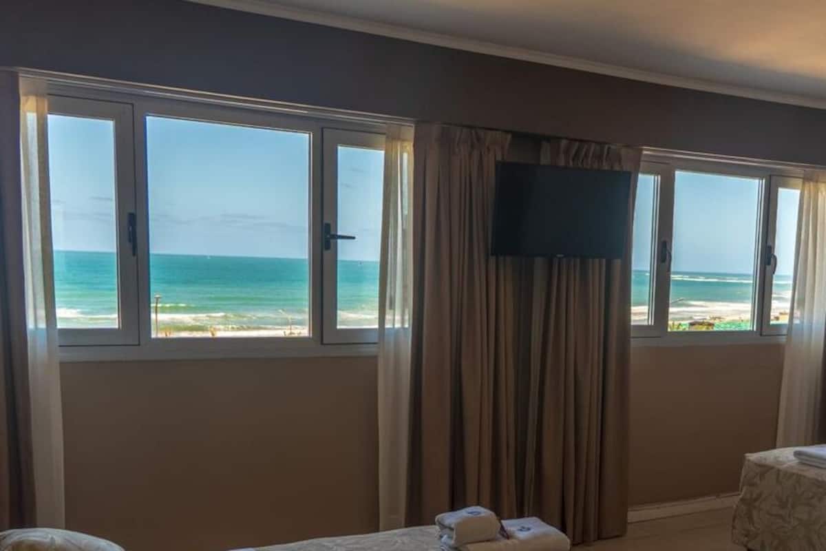 A hotel room with two beds, a TV, and a view of the beach.