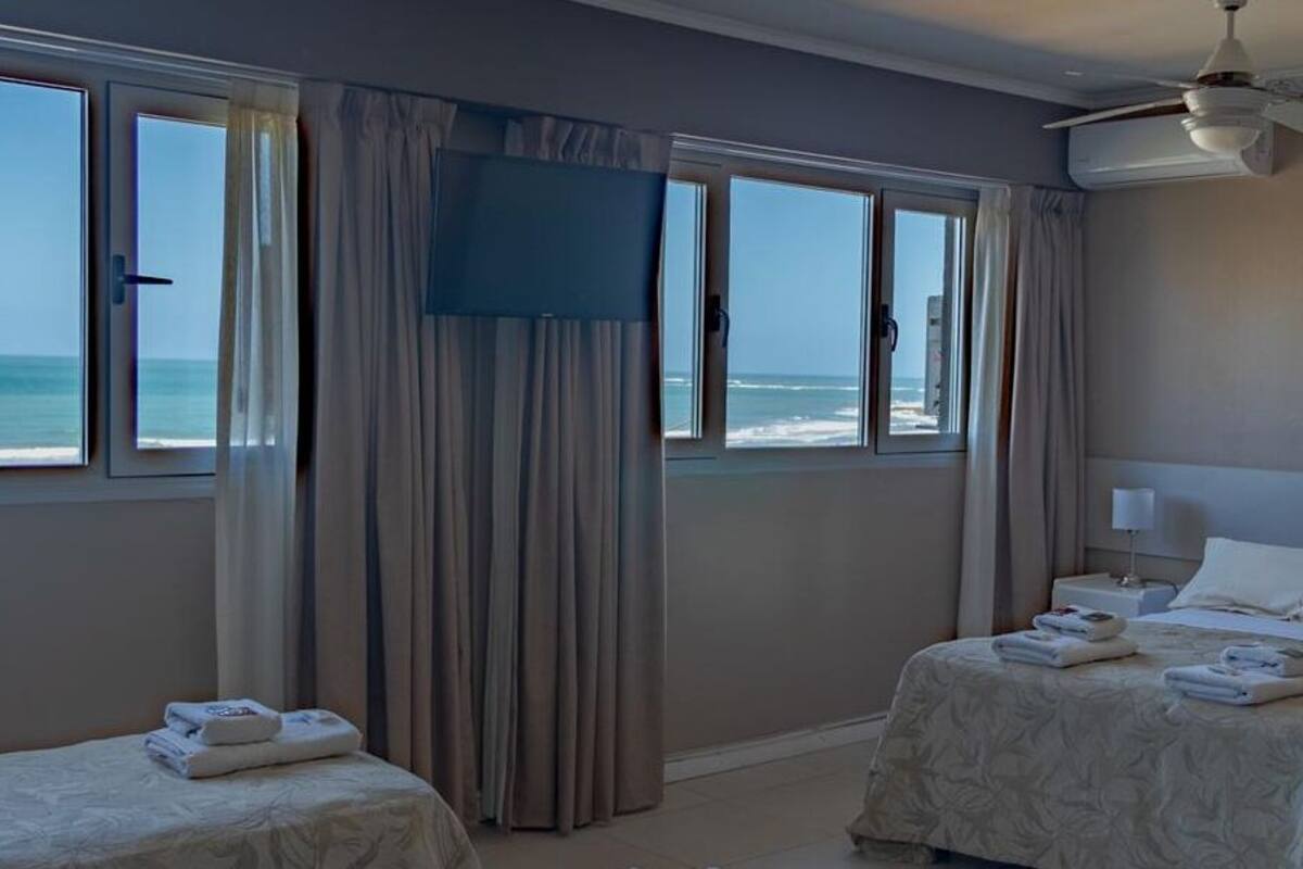 A hotel room with two beds, a TV, a ceiling fan, and a view of the ocean.