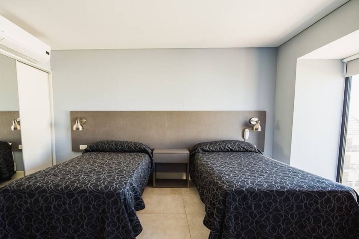 A room with two beds, a mirror, a window, and a wall-mounted air conditioning unit.