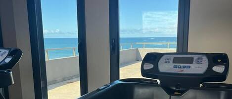 Un gimnasio con cinta de correr y bicicleta estática, amplias ventanas con vista al océano.
