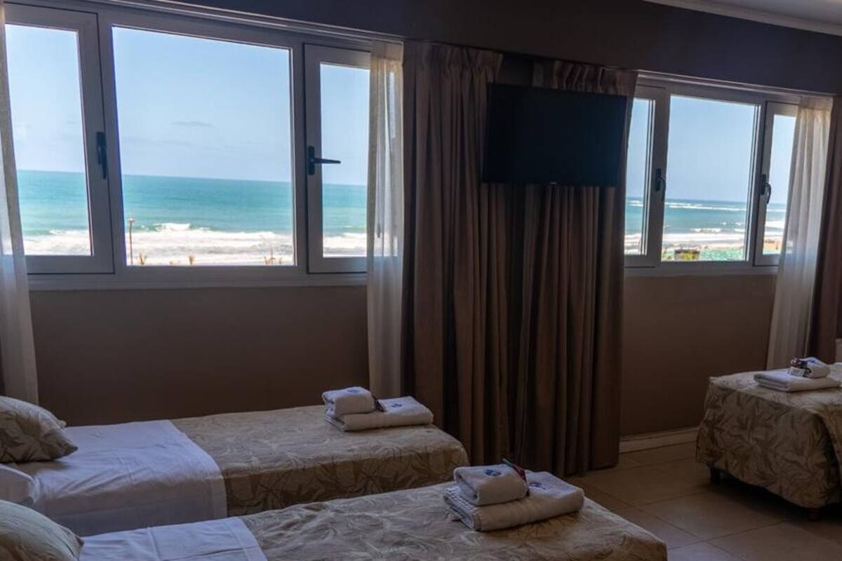 A hotel room with two beds, a TV, and a view of the beach.