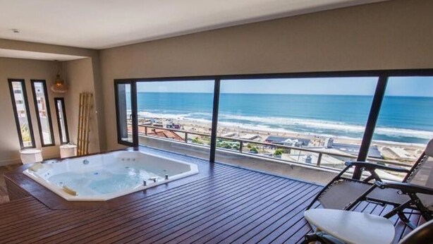Un balcón con hidromasaje, una silla y vista al océano.