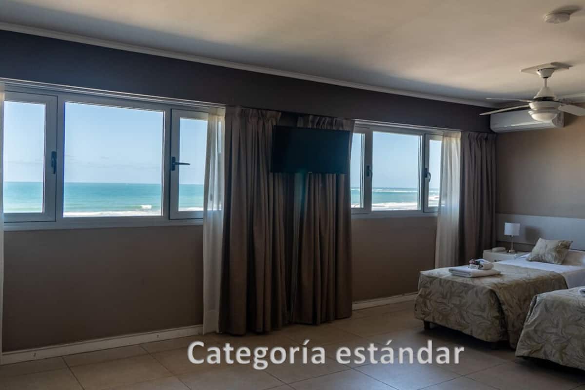 A hotel room with two beds, a TV, and a view of the beach.