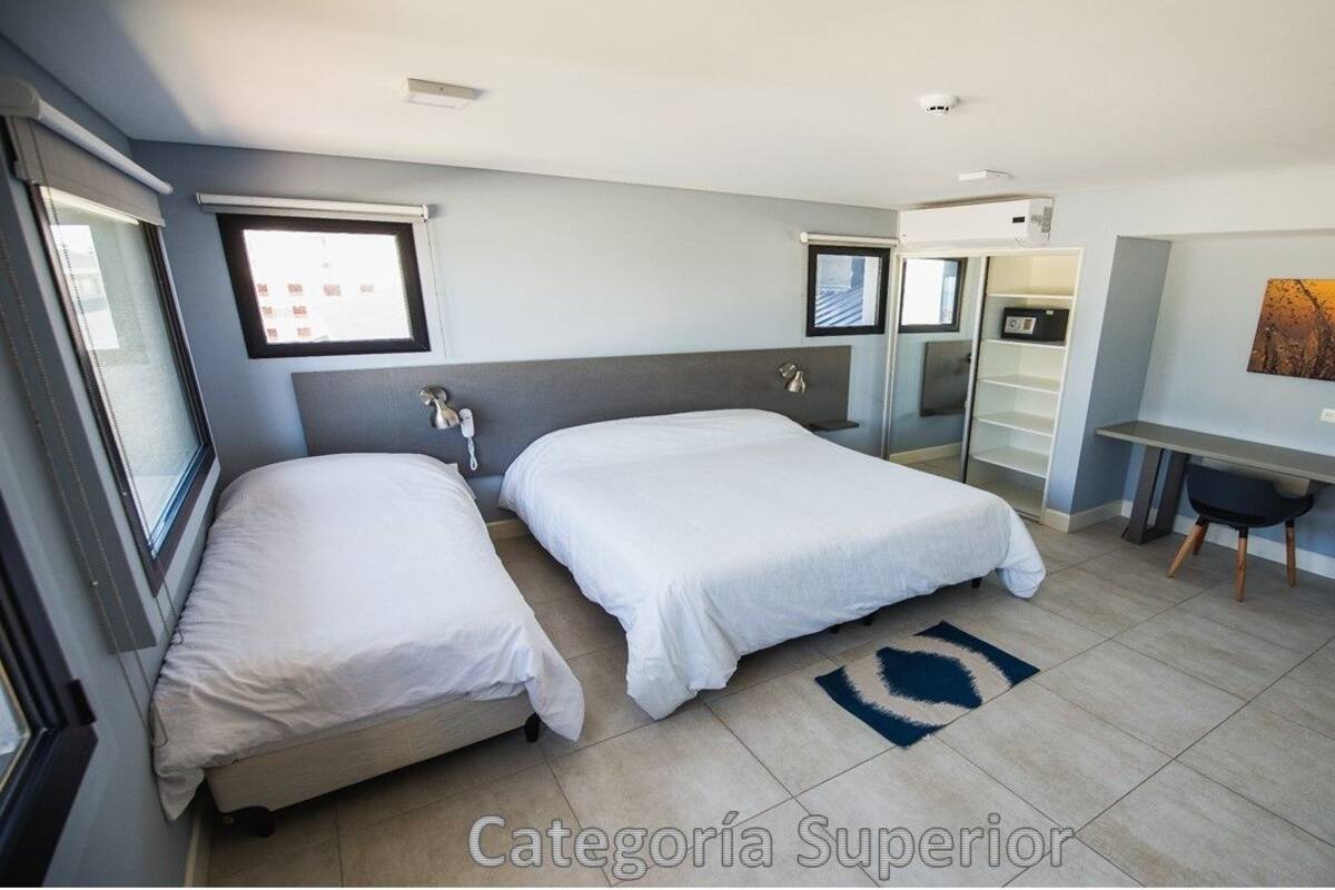 A modern hotel room with two beds, a desk, a chair, and a large window.