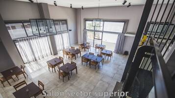 A spacious dining area with multiple tables and chairs, large windows, and a staircase.