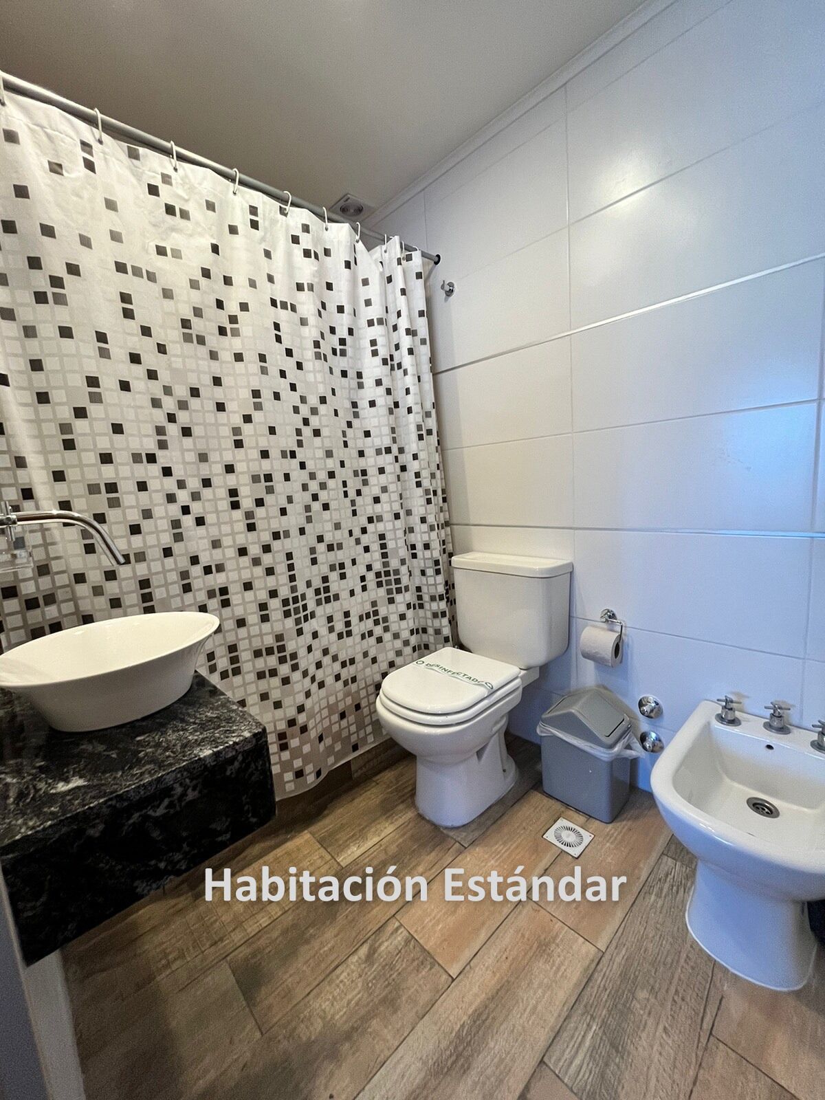 A standard bathroom with a tiled floor, a white toilet, a sink, and a shower curtain with a geometric pattern.