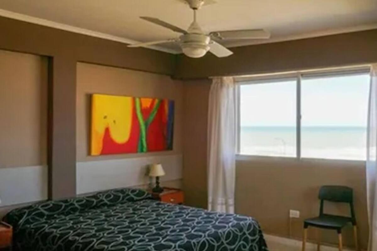 A bedroom with a bed, a ceiling fan, a window with a view, and a colorful painting on the wall.
