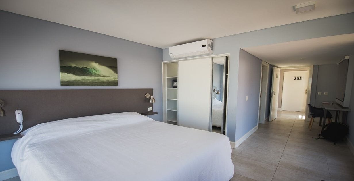 Habitación de hotel con una cama grande, un armario, un escritorio y un baño visible a través de una puerta abierta.