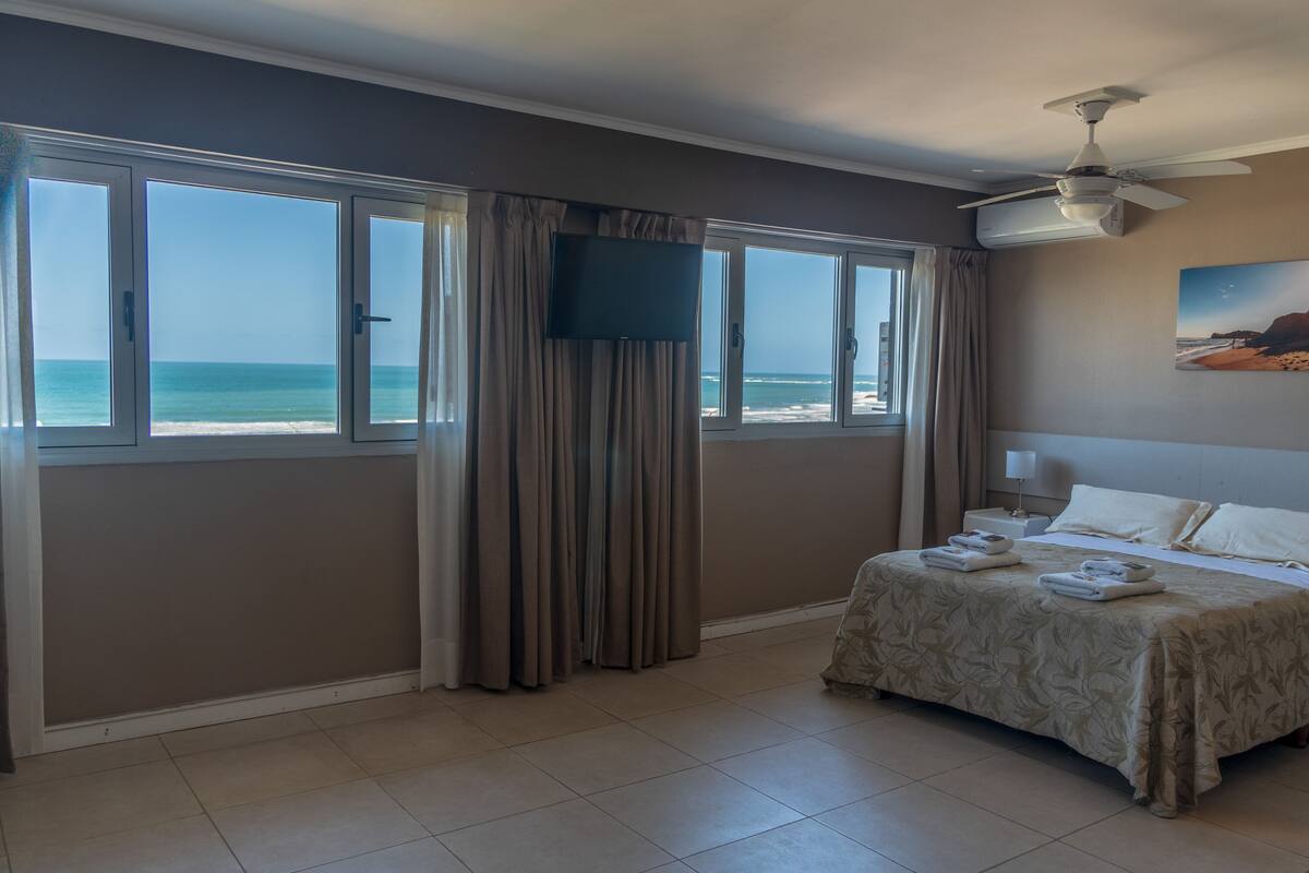 A hotel room with a bed, a TV, a ceiling fan, and a view of the ocean.