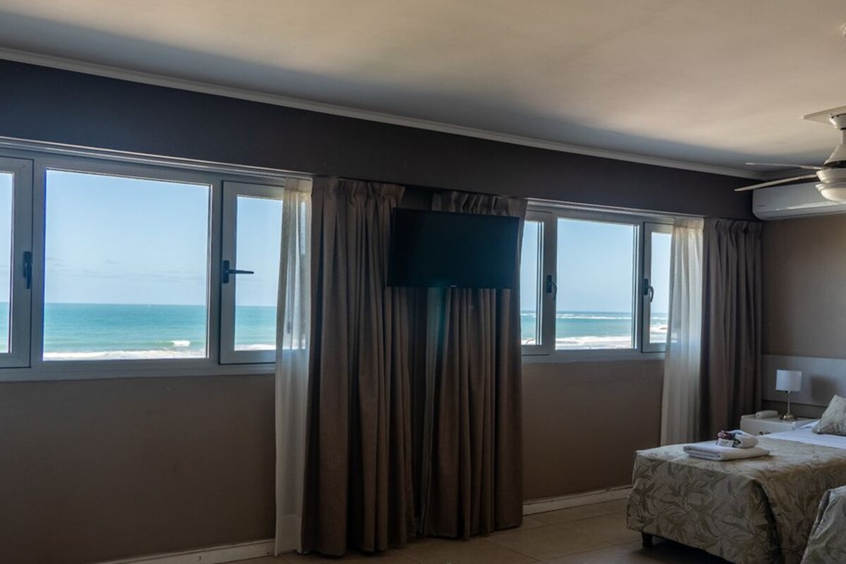 A hotel room with two beds, a TV, and a view of the beach.