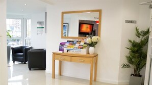 A reception area with a wooden desk, a mirror, a television, and a potted plant. - Hotel Express Newcastle Gateshead (Gateshead)