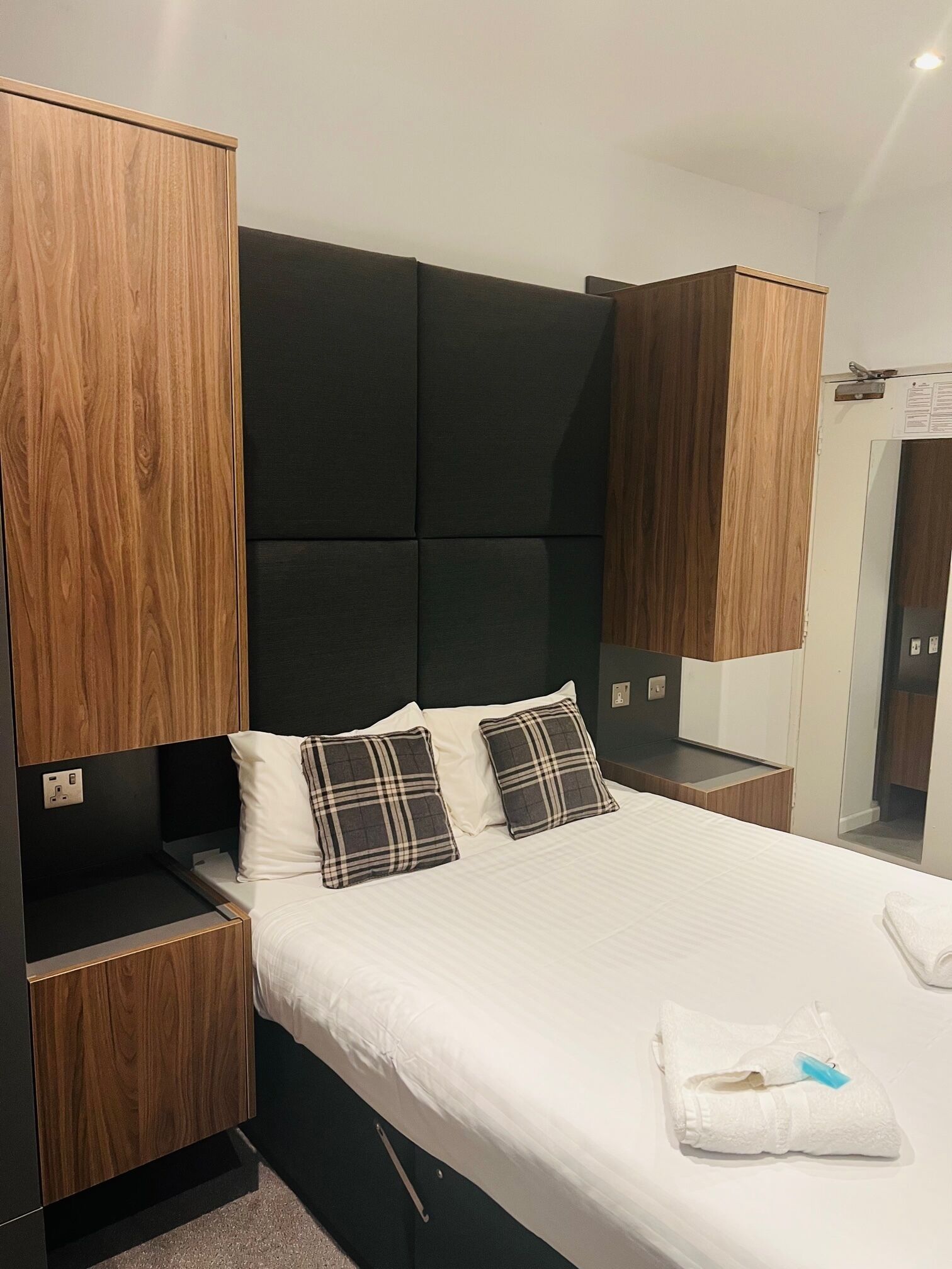 A hotel room with a bed, wooden headboard, two bedside tables, and a wardrobe.
