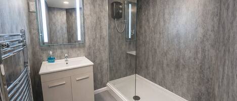 A modern bathroom with a glass-enclosed shower, a white sink with a mirror above it, and a towel rack with a towel dispenser.