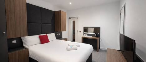 Una habitación de hotel moderna con una cama grande, televisión, escritorio y armario.