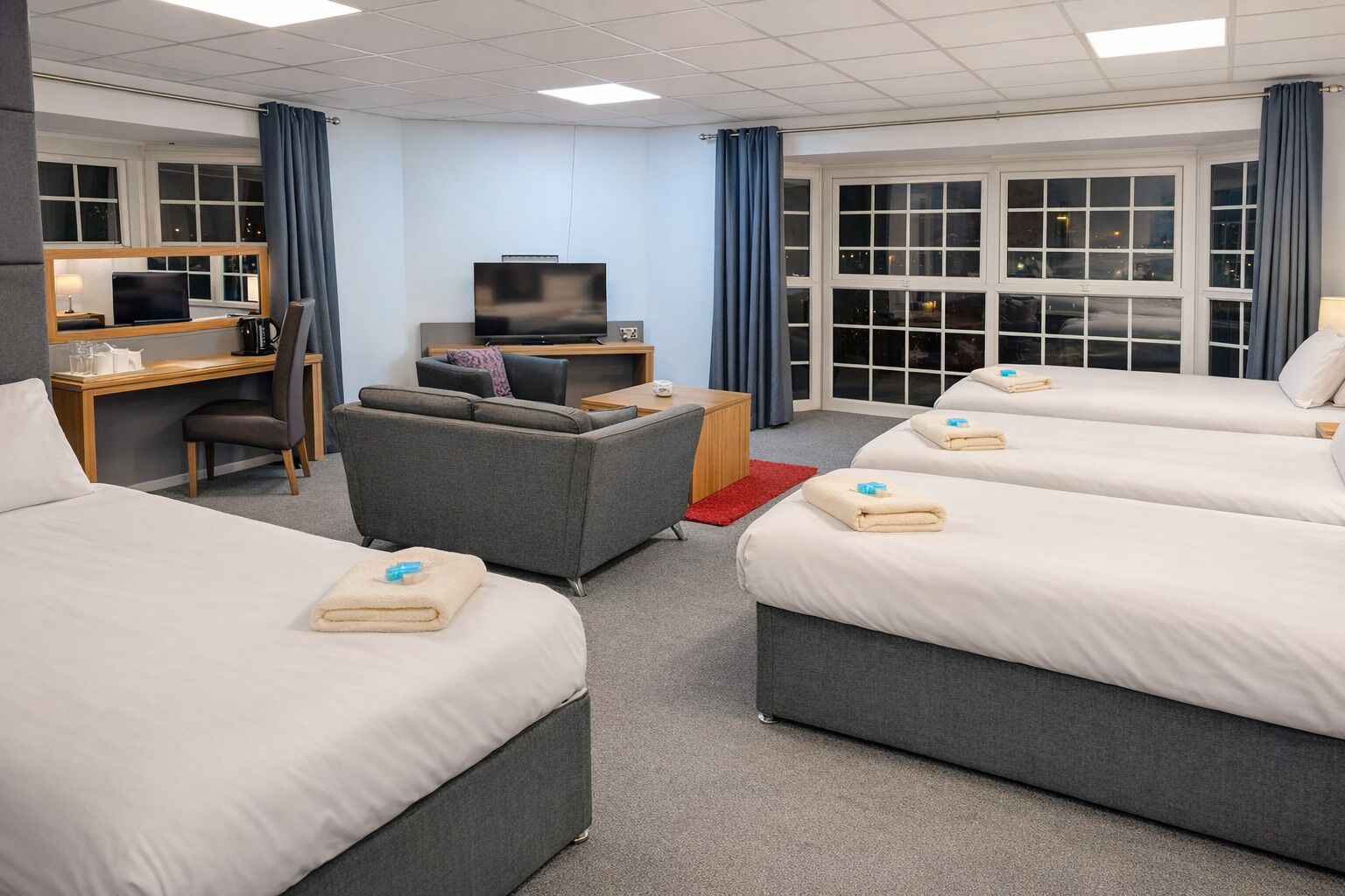 A hotel room with two beds, a desk, a television, and a sofa.