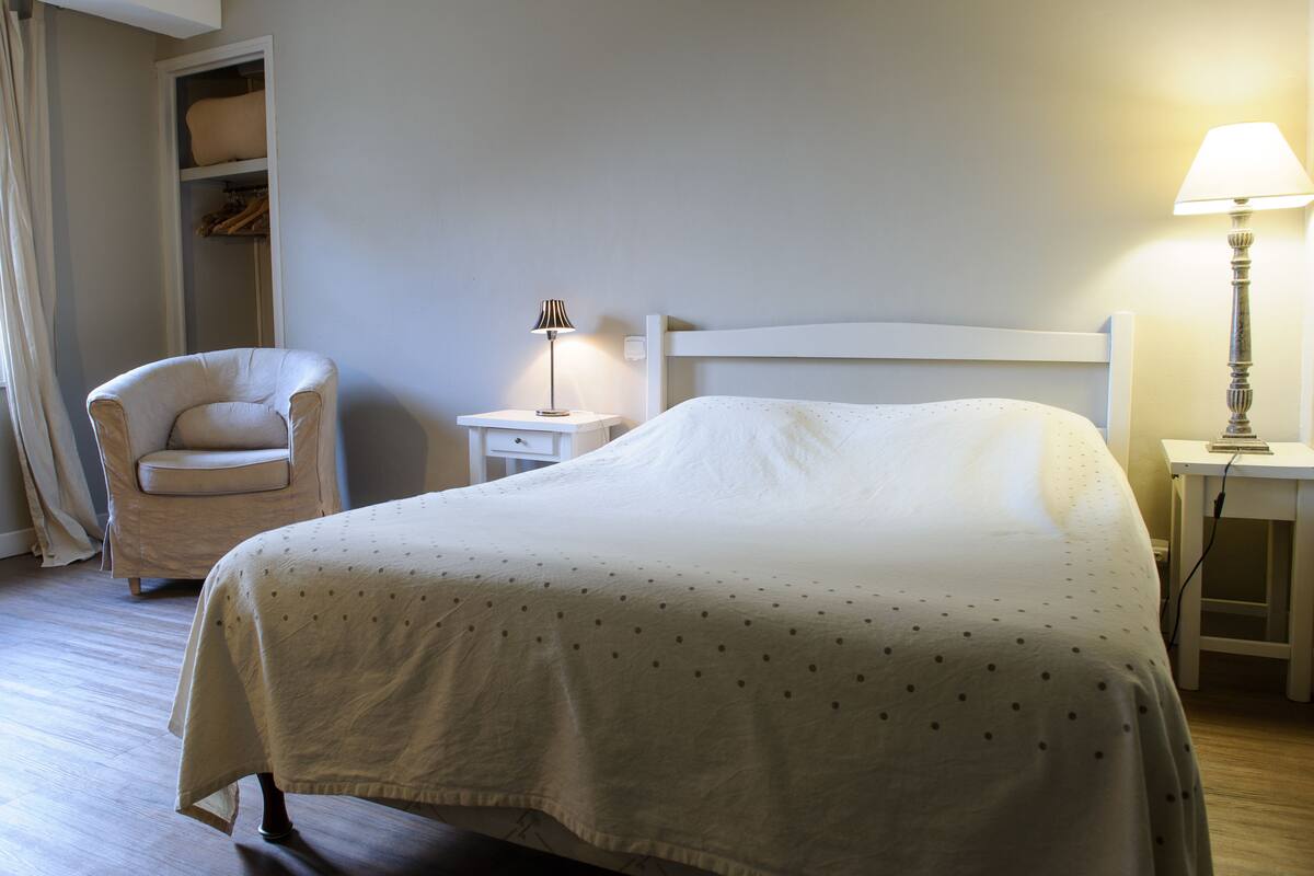A neatly arranged bedroom with a bed, a chair, a bedside table with a lamp, and a wardrobe.