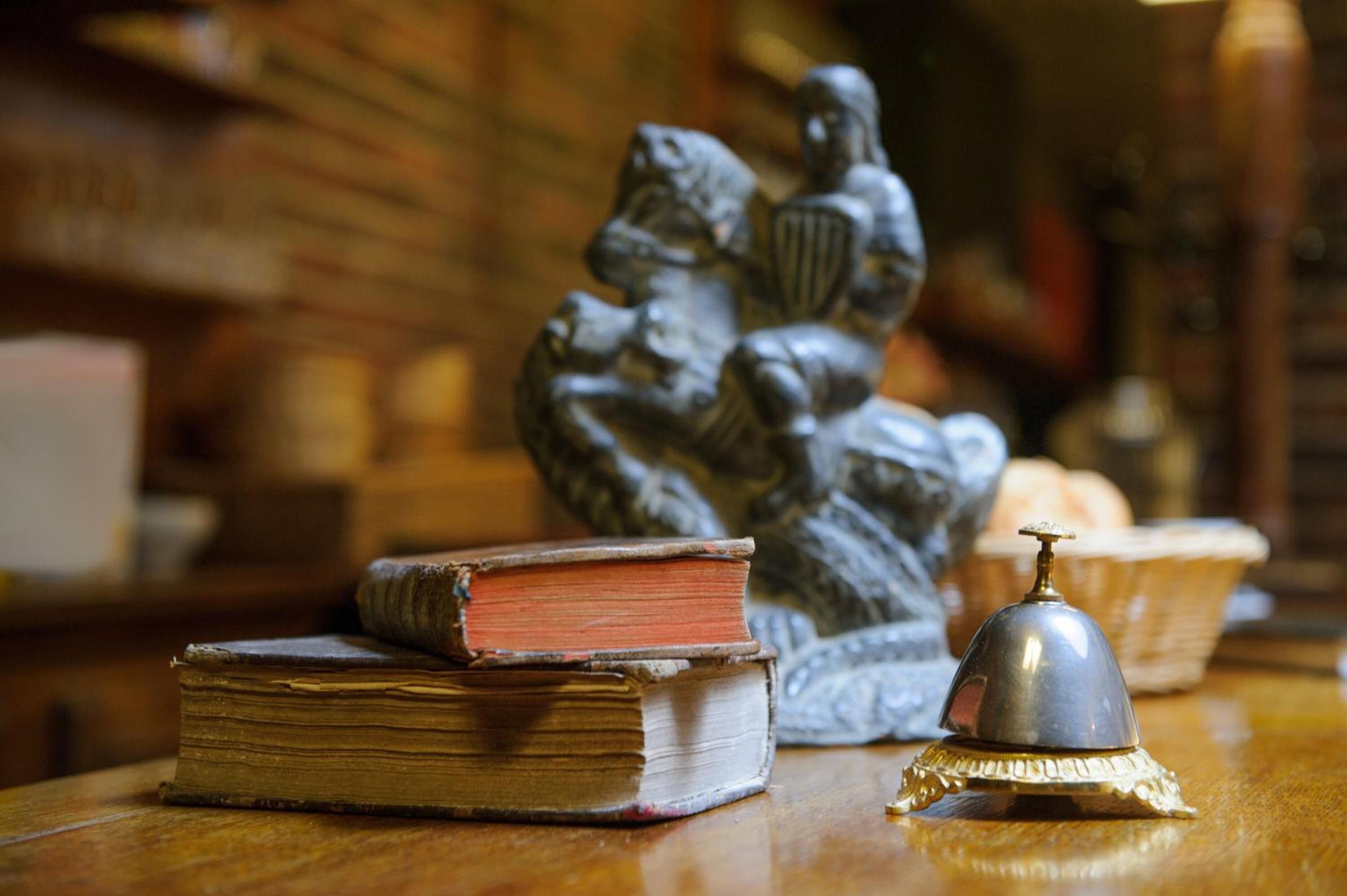 A wooden table with a stack of old books, a metal bell, and a statue.