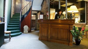 A reception desk in a hotel lobby with a staircase, a fire extinguisher, and a potted plant.