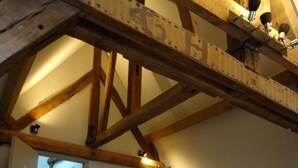 A bedroom with a sloped ceiling, wooden beams, a bed, a nightstand, a lamp, and a table with towels.