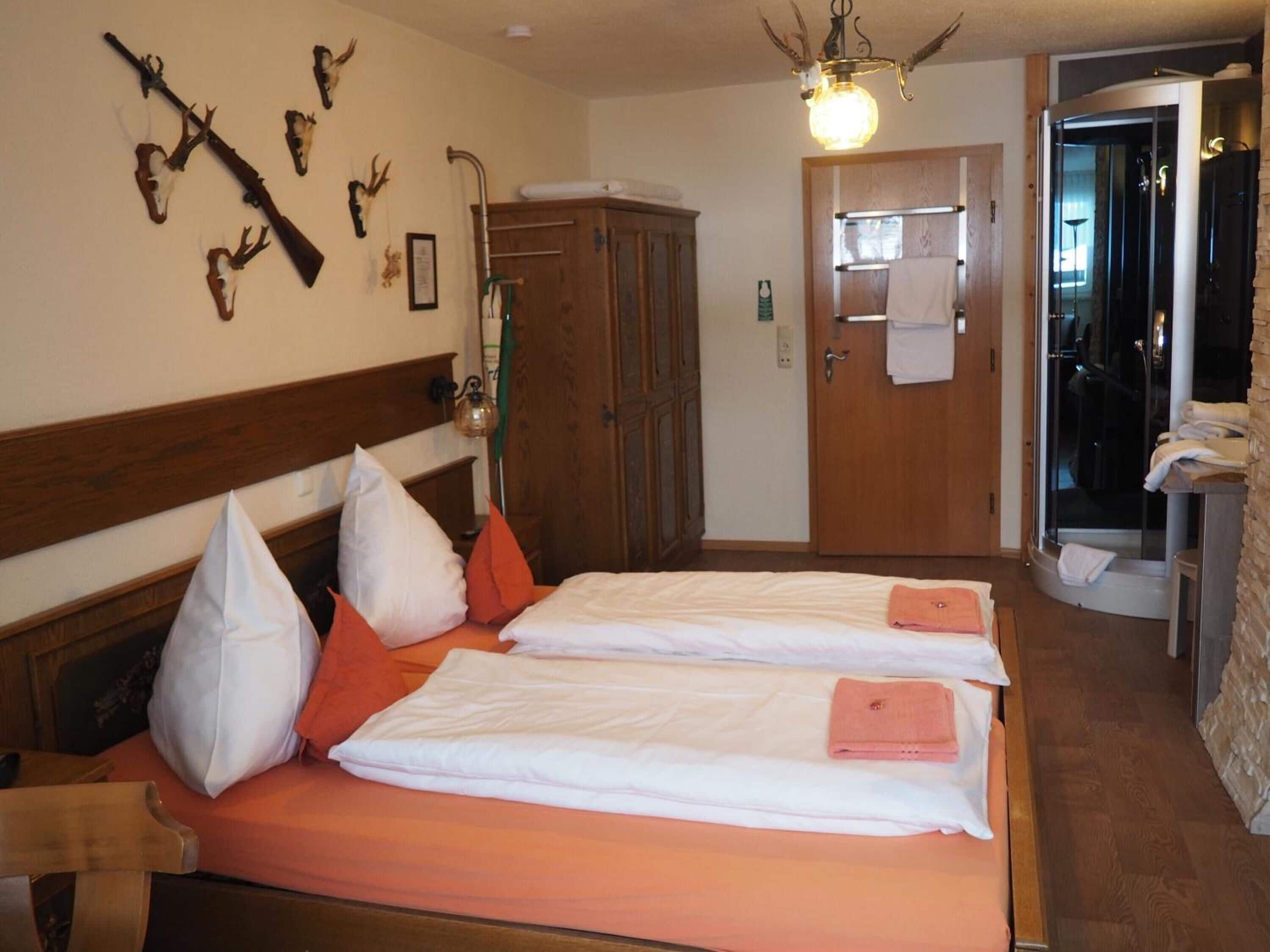 Ein Hotelzimmer mit zwei Betten, einem hölzernen Kopfteil, einem an der Wand befestigten Hirschgeweih und einer Duschkabine mit Glastür.