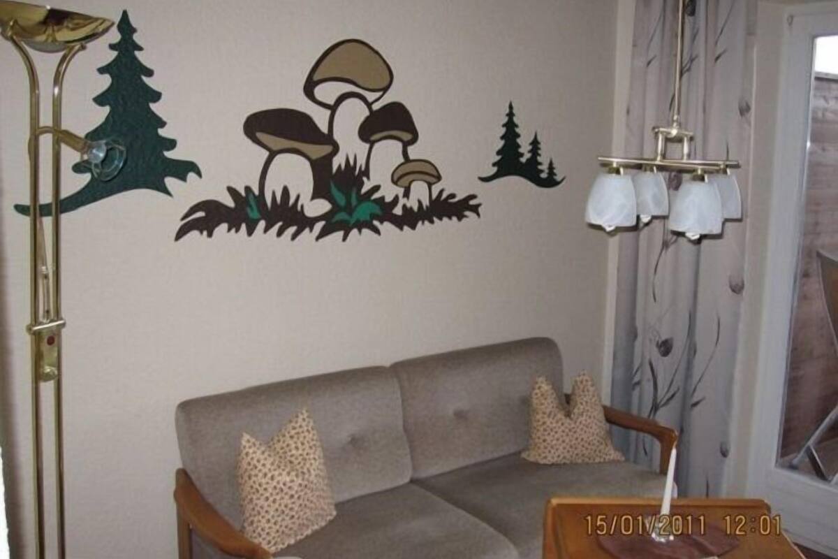 A living room with a grey sofa, decorative wall art, a lamp, and a window with curtains.