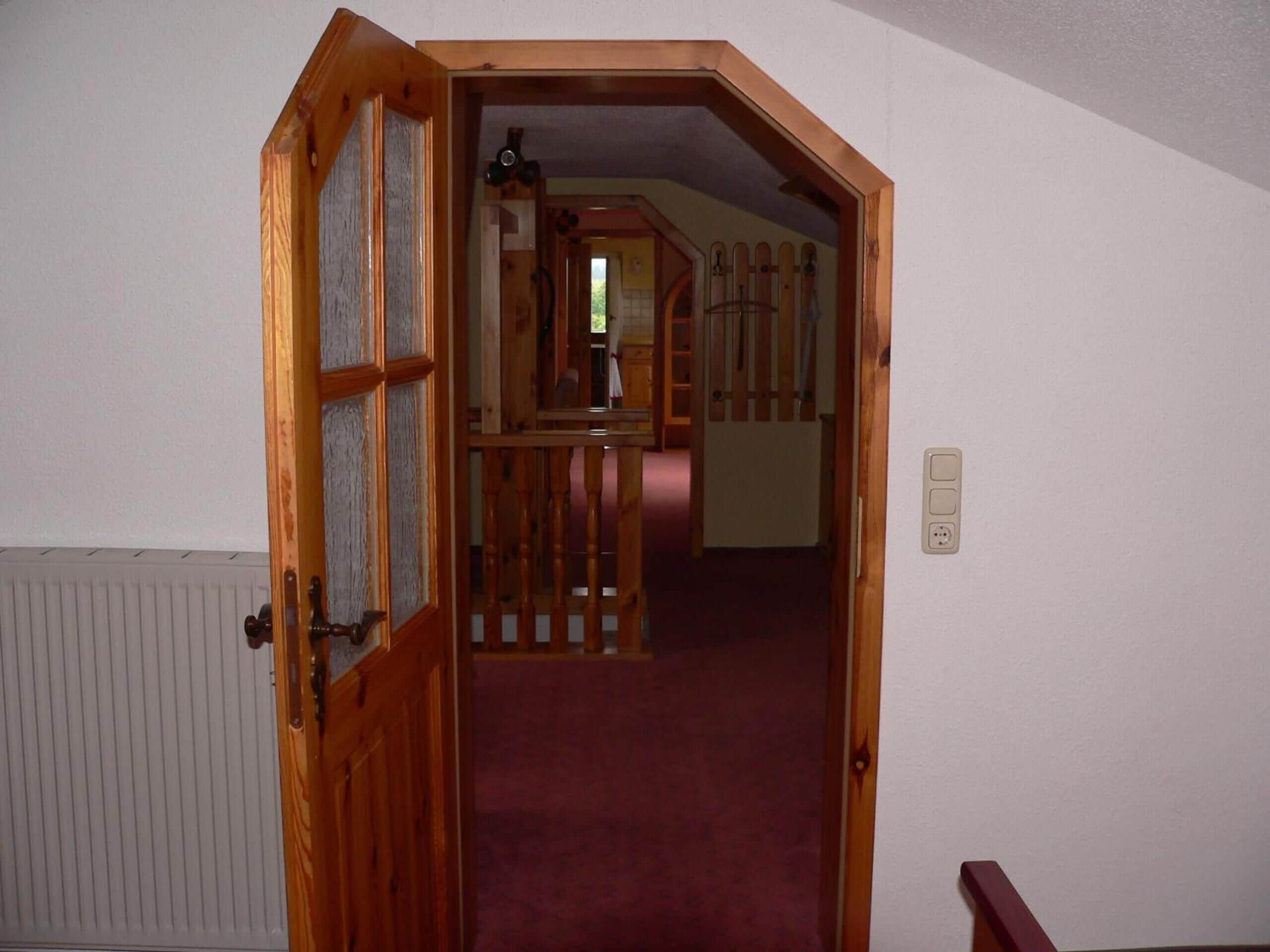 A wooden door leading to a hallway with a red carpet.
