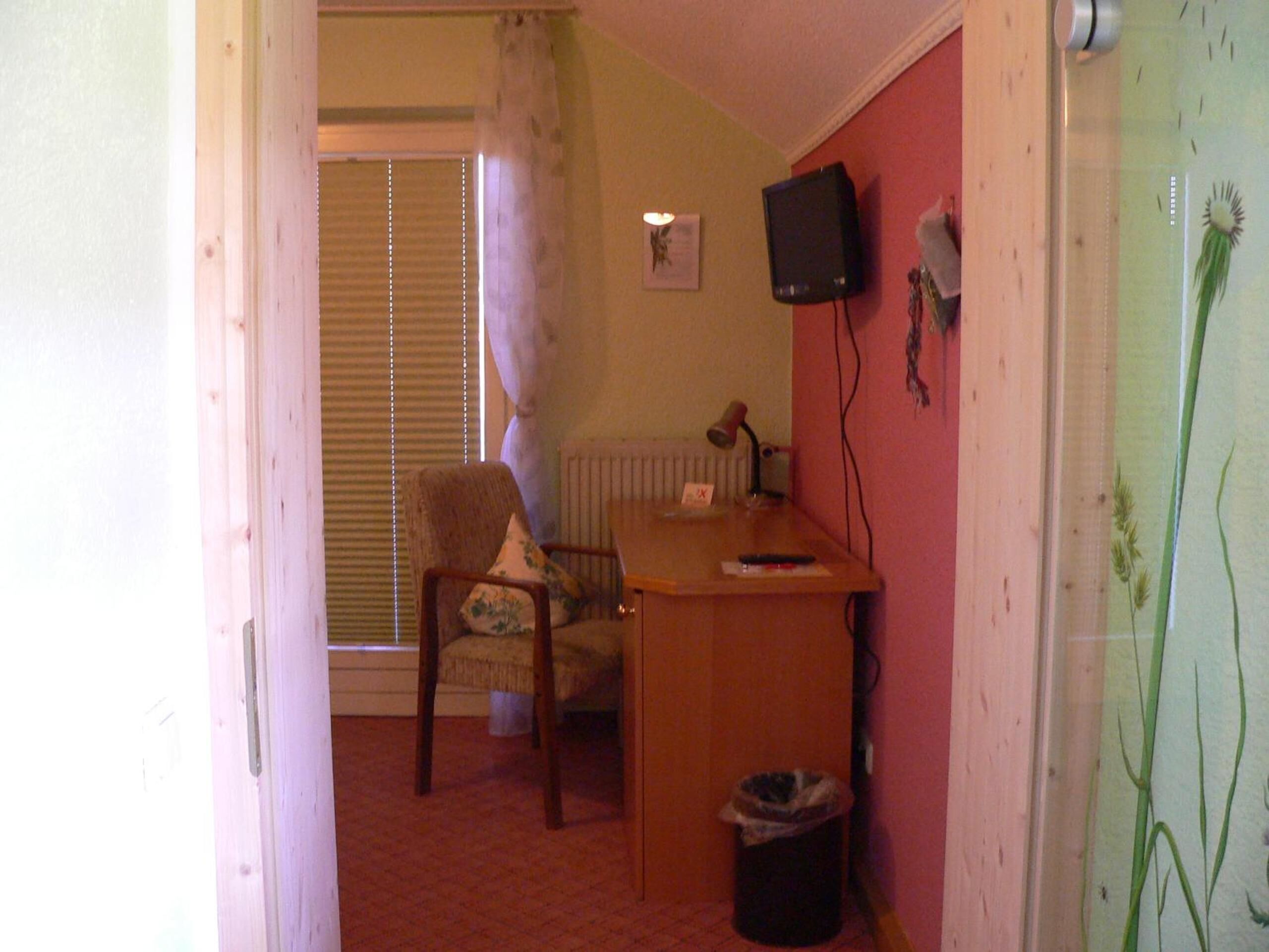 A small room with a wooden desk, a chair, a radiator, a television, and a trash bin.