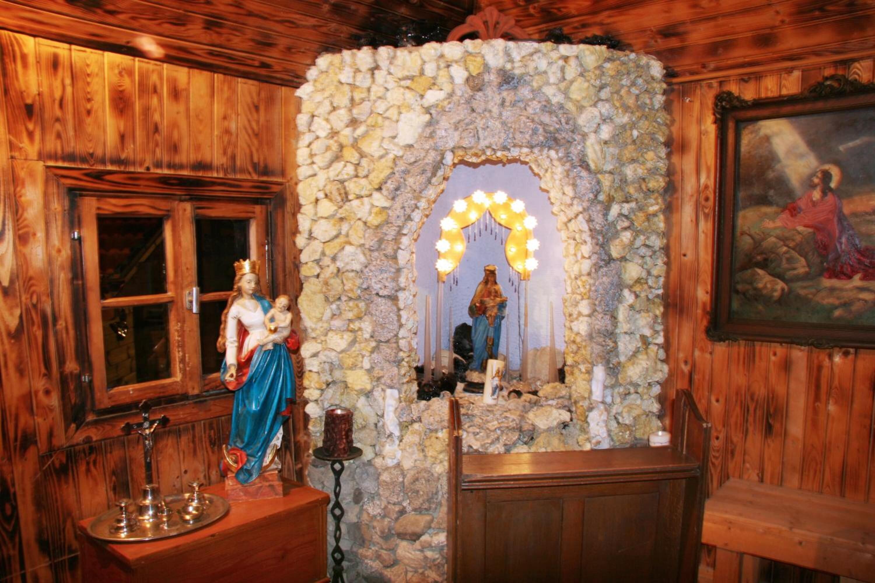 A wooden interior with a stone altar, a statue, and a painting.
