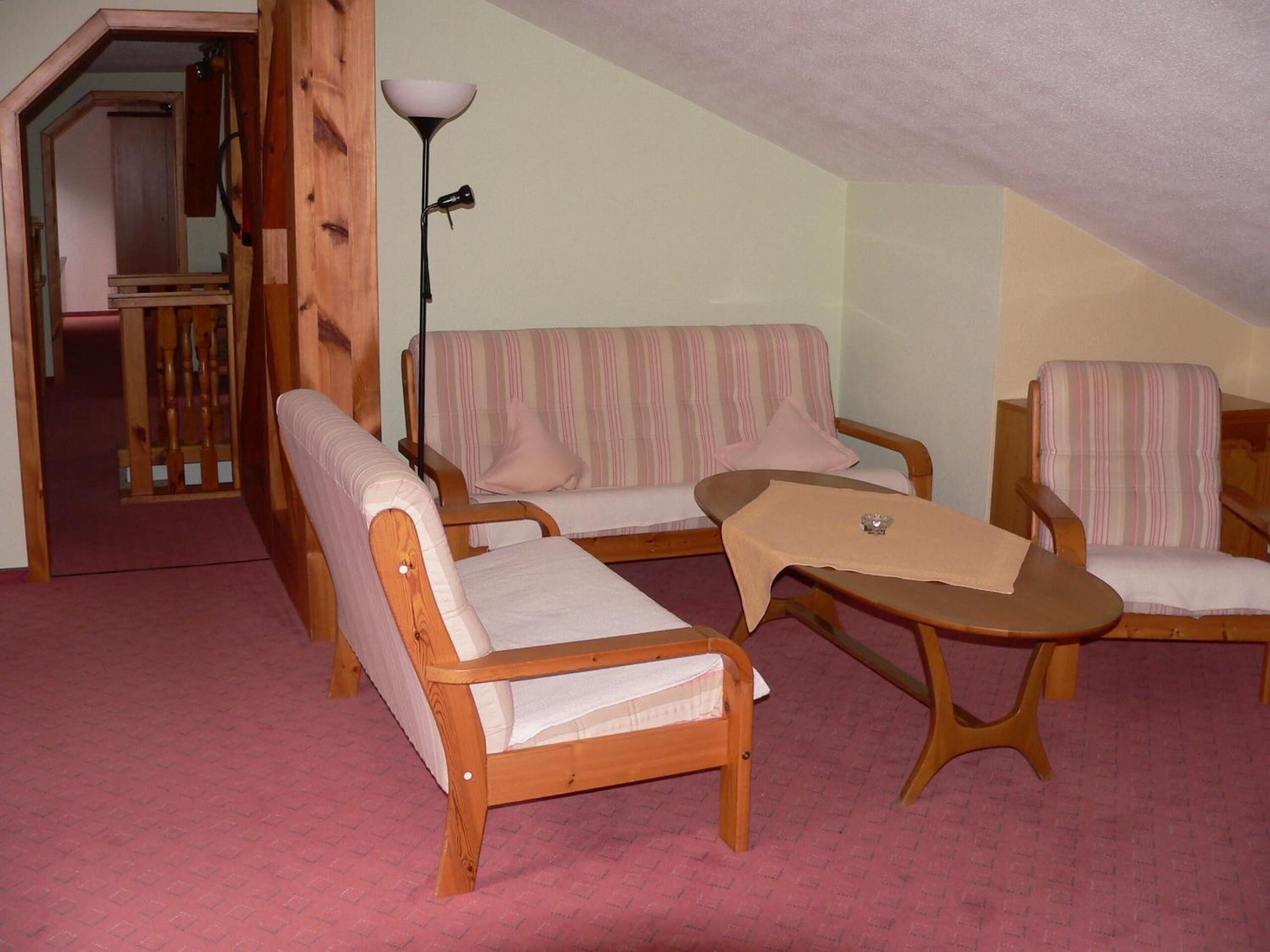 A cozy attic room with a wooden staircase, a striped sofa, two armchairs, and a small table.