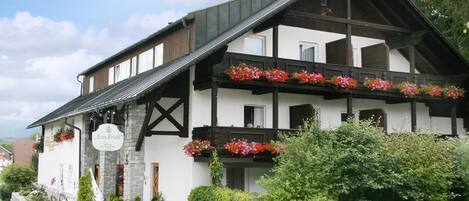 A traditional European hotel with a stone facade, multiple balconies with flower boxes, and outdoor seating.