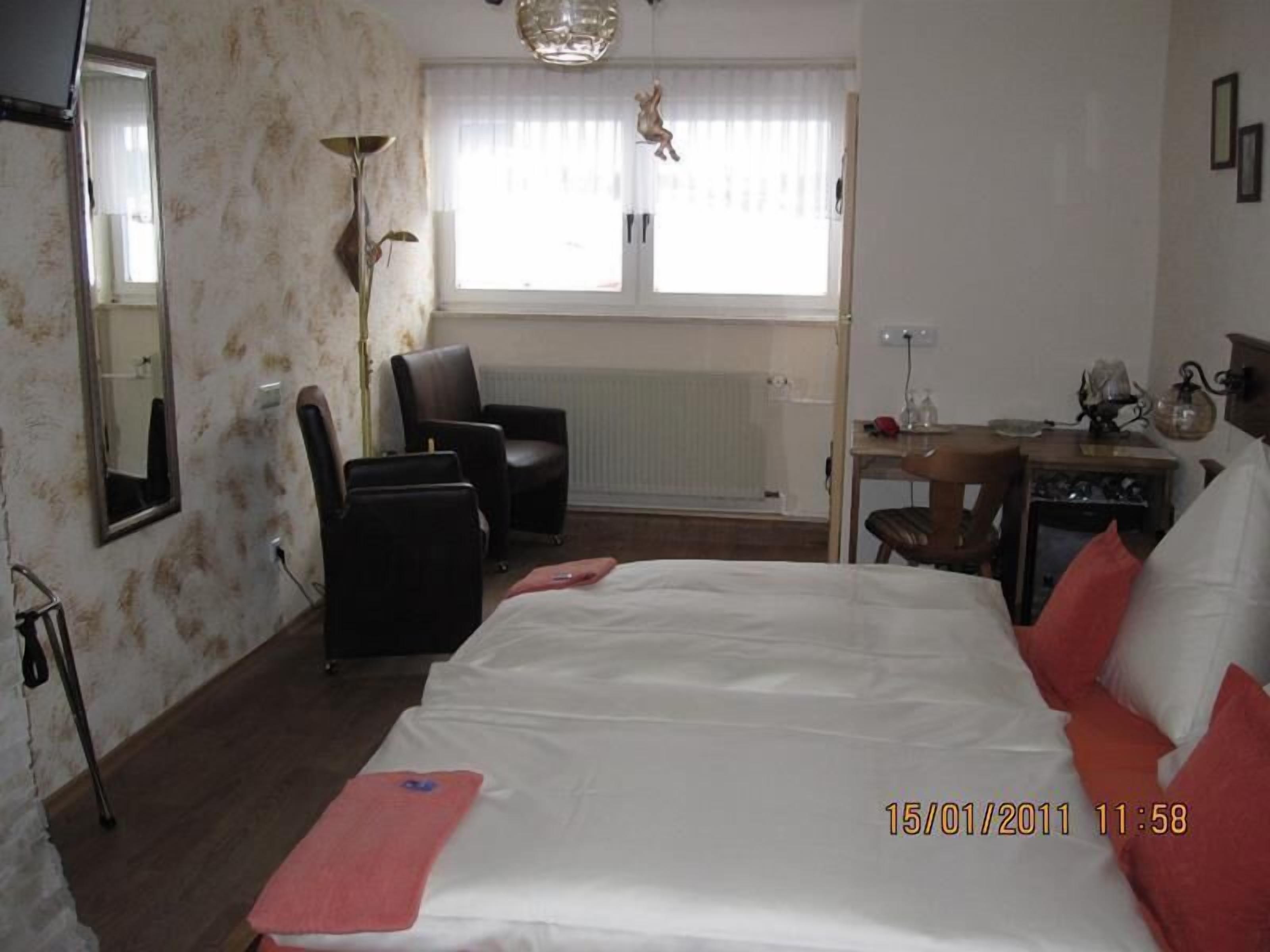 A hotel room with a large bed, a desk, a chair, a radiator, and a window with curtains.