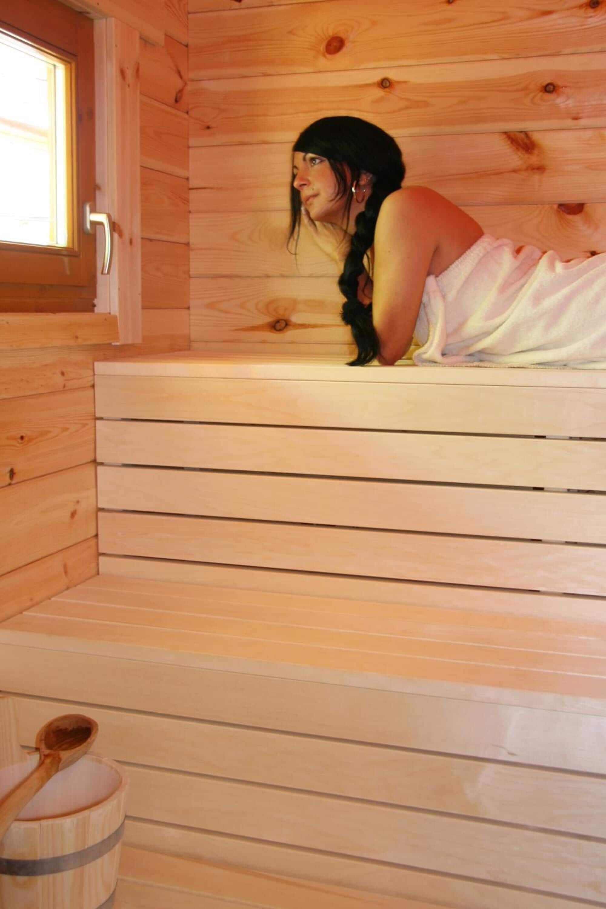 Puuinen sauna, jossa on penkki ja puinen ämpäri.