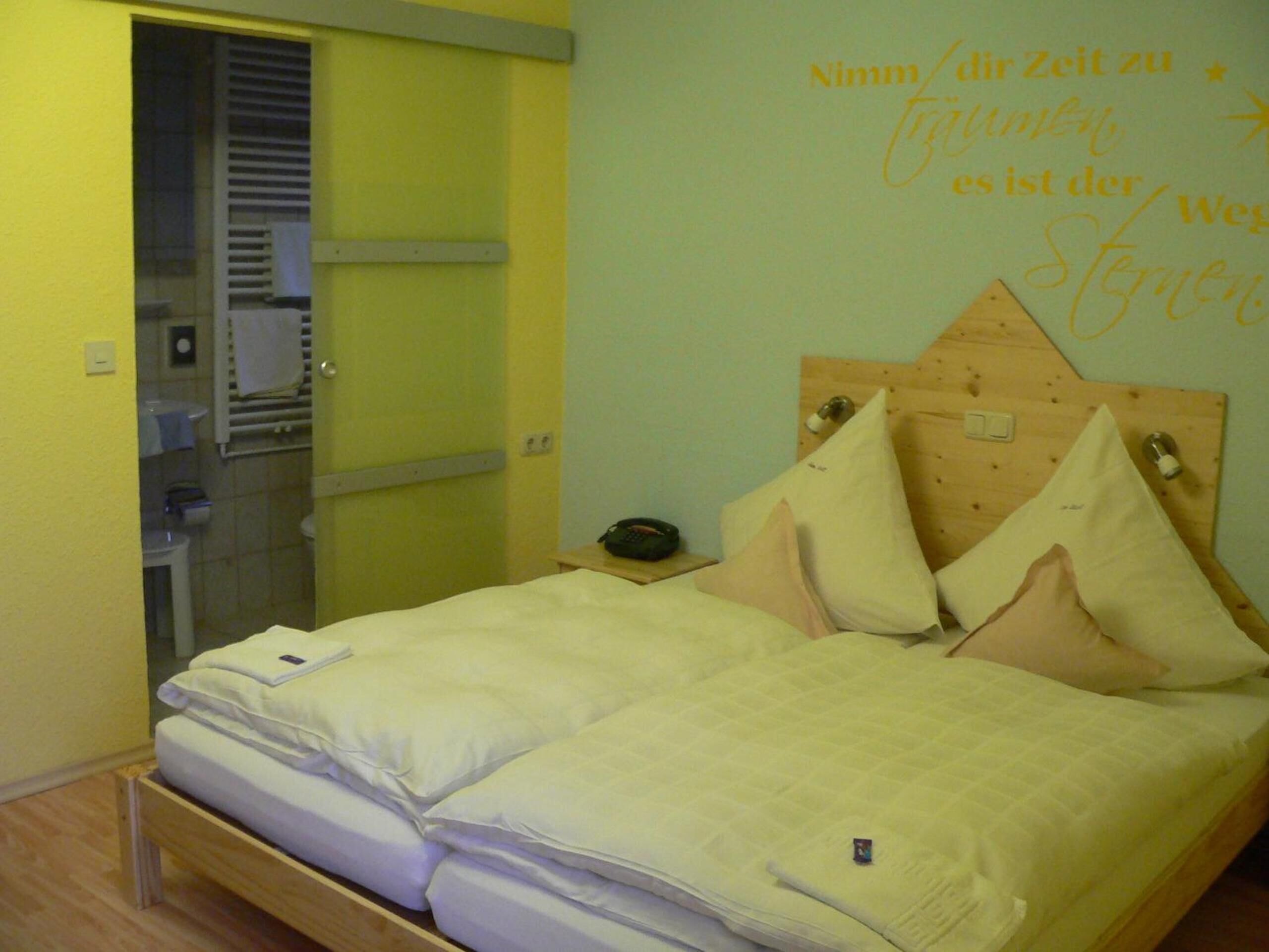 Una cama con cabecera de madera, una mesita de noche y una pared con un letrero decorativo.