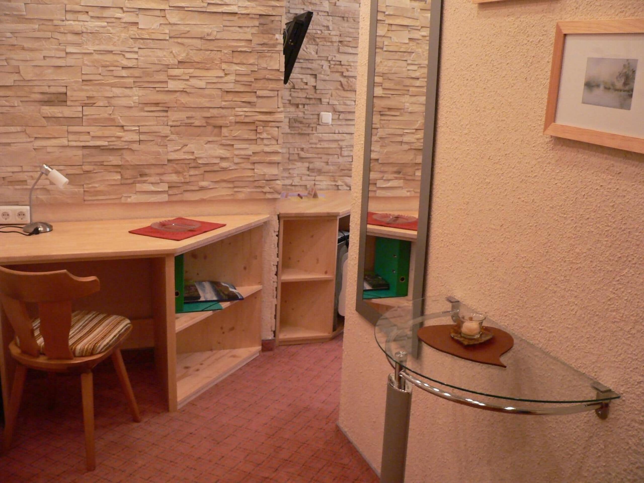 A study room with a wooden desk, a chair, a mirror, and shelves.