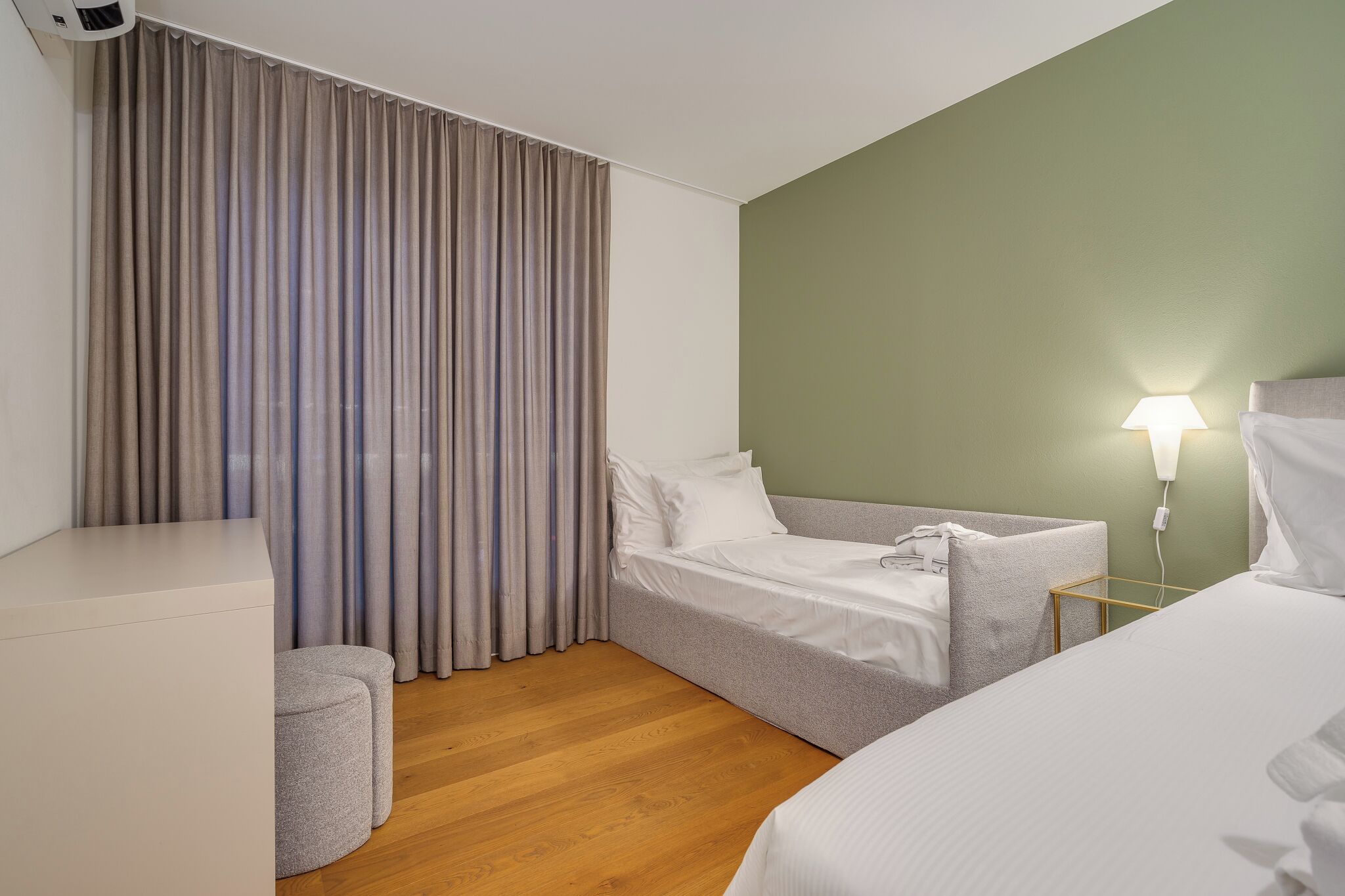 A hotel room with a bed, a seating area, a lamp, and a window with curtains.