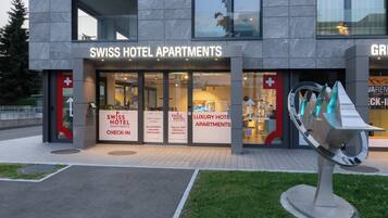 A modern building with a sign for Swiss Hotel Apartments. There are multiple signs in different languages welcoming guests.