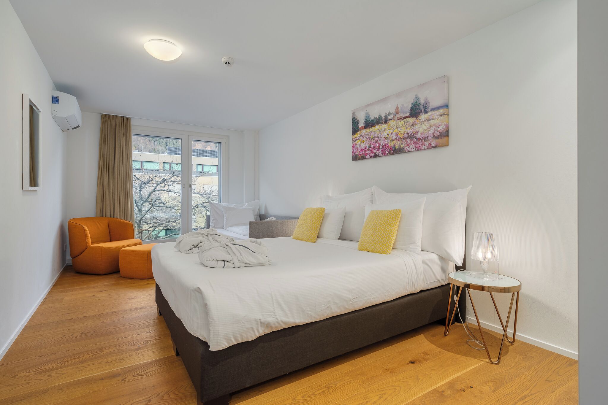 A modern bedroom with a large bed, a side table, a chair, and a painting on the wall.