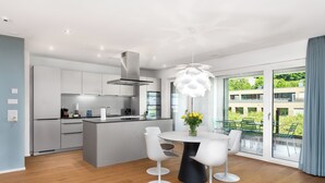 A modern kitchen with white cabinetry, a central island, and a dining area with a round table and four chairs. - Swiss Hotel Apartments-Interlaken (Interlaken)