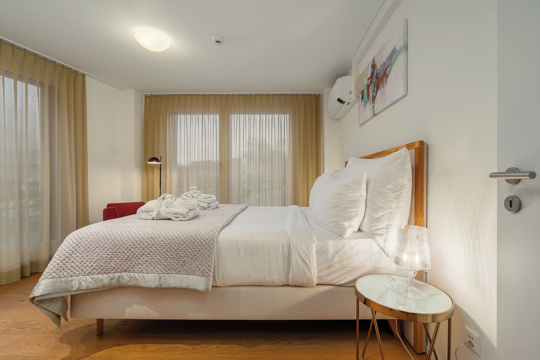 Un dormitorio ordenado con cama, mesita de noche y ventana con cortinas.