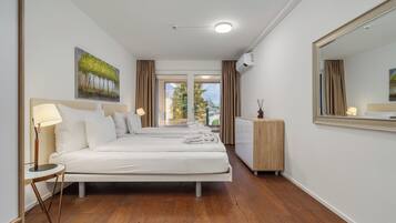 Een hotelkamer met twee bedden, een grote spiegel, een houten vloer en uitzicht op bomen door het raam.