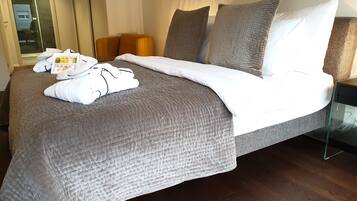 A neatly made bed with a grey quilt, white pillows, and a white blanket. There is a tray with toiletries on the bed.