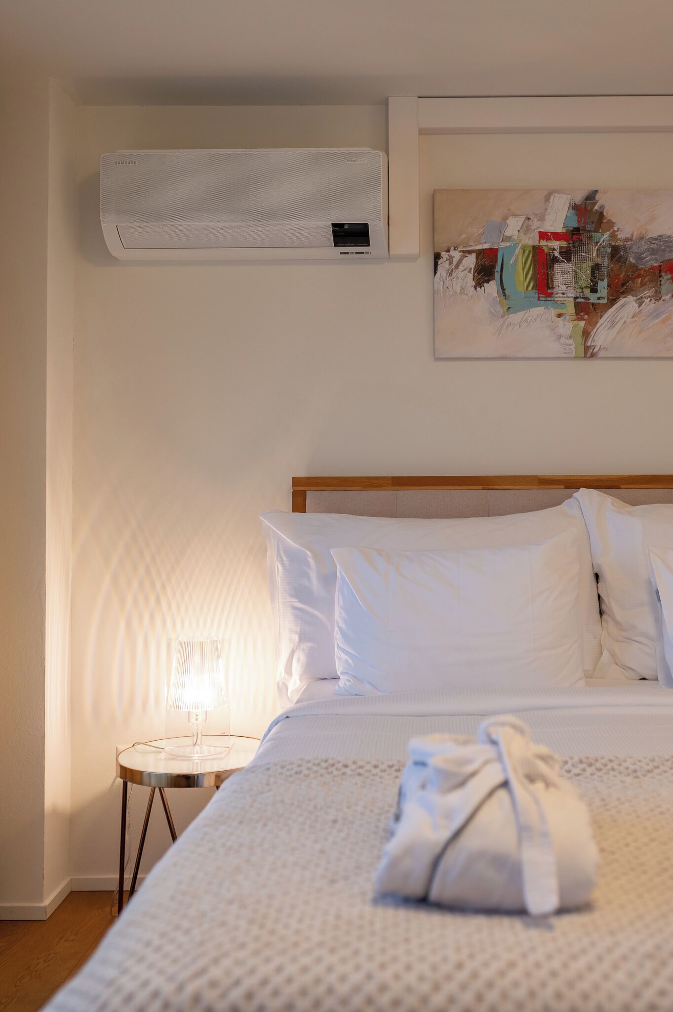Une chambre d’hôtel avec un lit, une table de chevet avec une lampe, un appareil de climatisation et un tableau au mur.