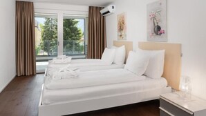 A hotel room with two beds, a large window with curtains, an air conditioning unit, and artwork on the wall. - Swiss Hotel Apartments-Interlaken (Interlaken)