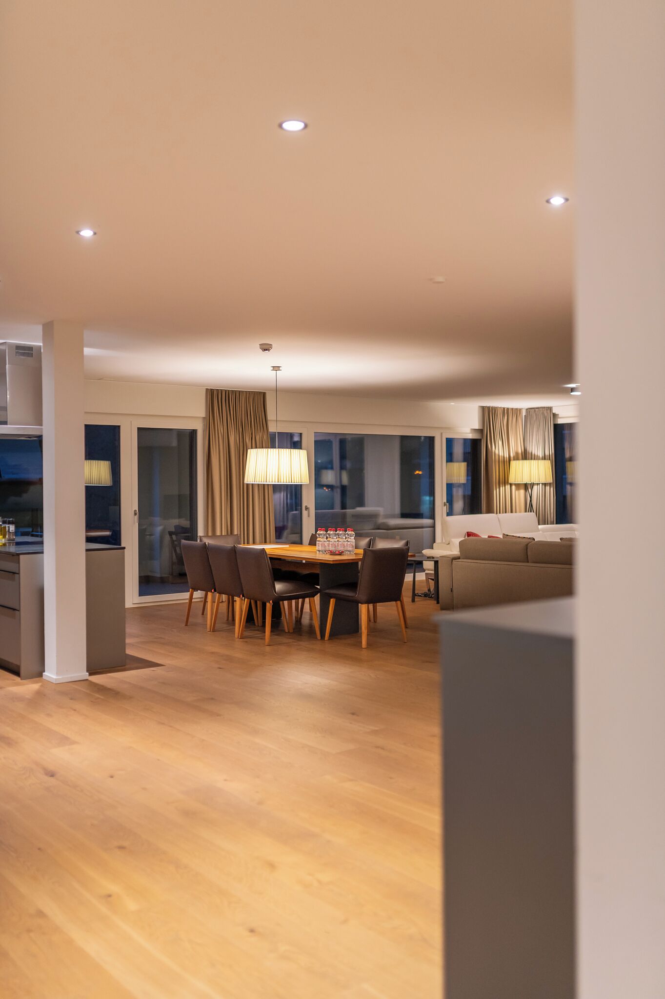 A modern living room with a dining area, featuring a wooden floor, a sofa, a dining table with chairs, and a large lamp.