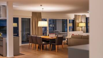 A modern living room with a dining area, featuring a wooden floor, a sofa, a dining table with chairs, and a large lamp.