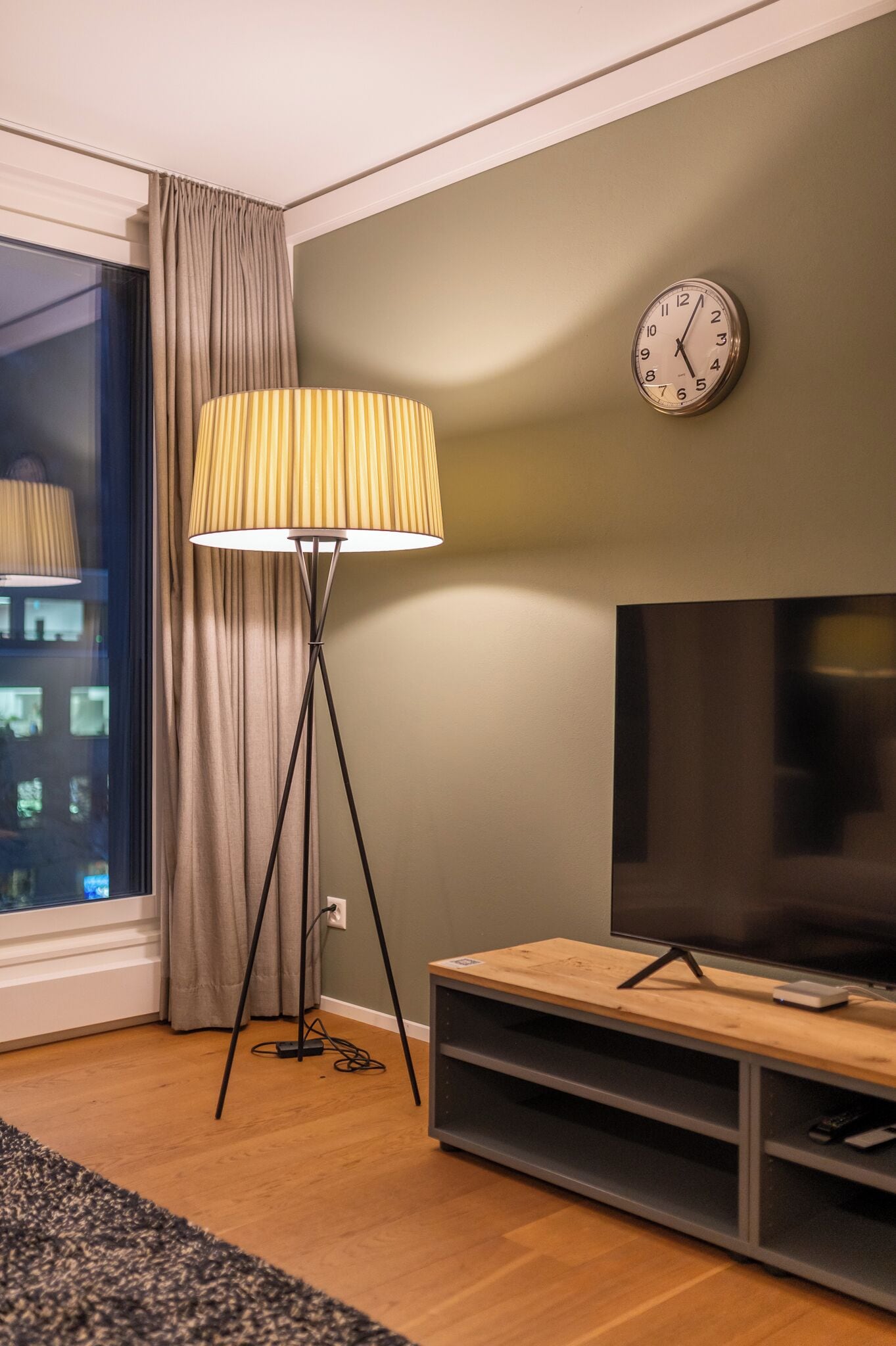 A modern living room with a floor lamp, a flat-screen TV, and a clock on the wall.