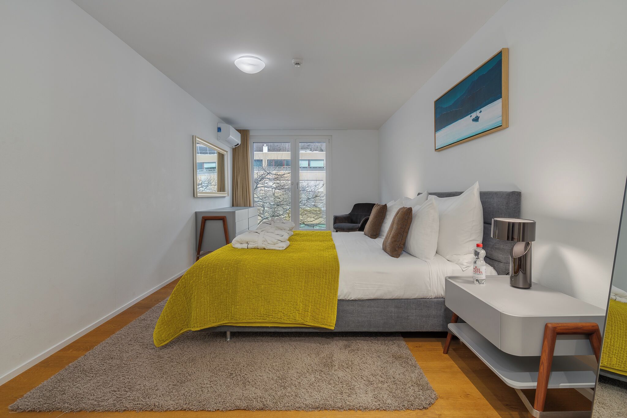 Um quarto moderno com uma cama, mesa de cabeceira e janela com vista para edifícios.
